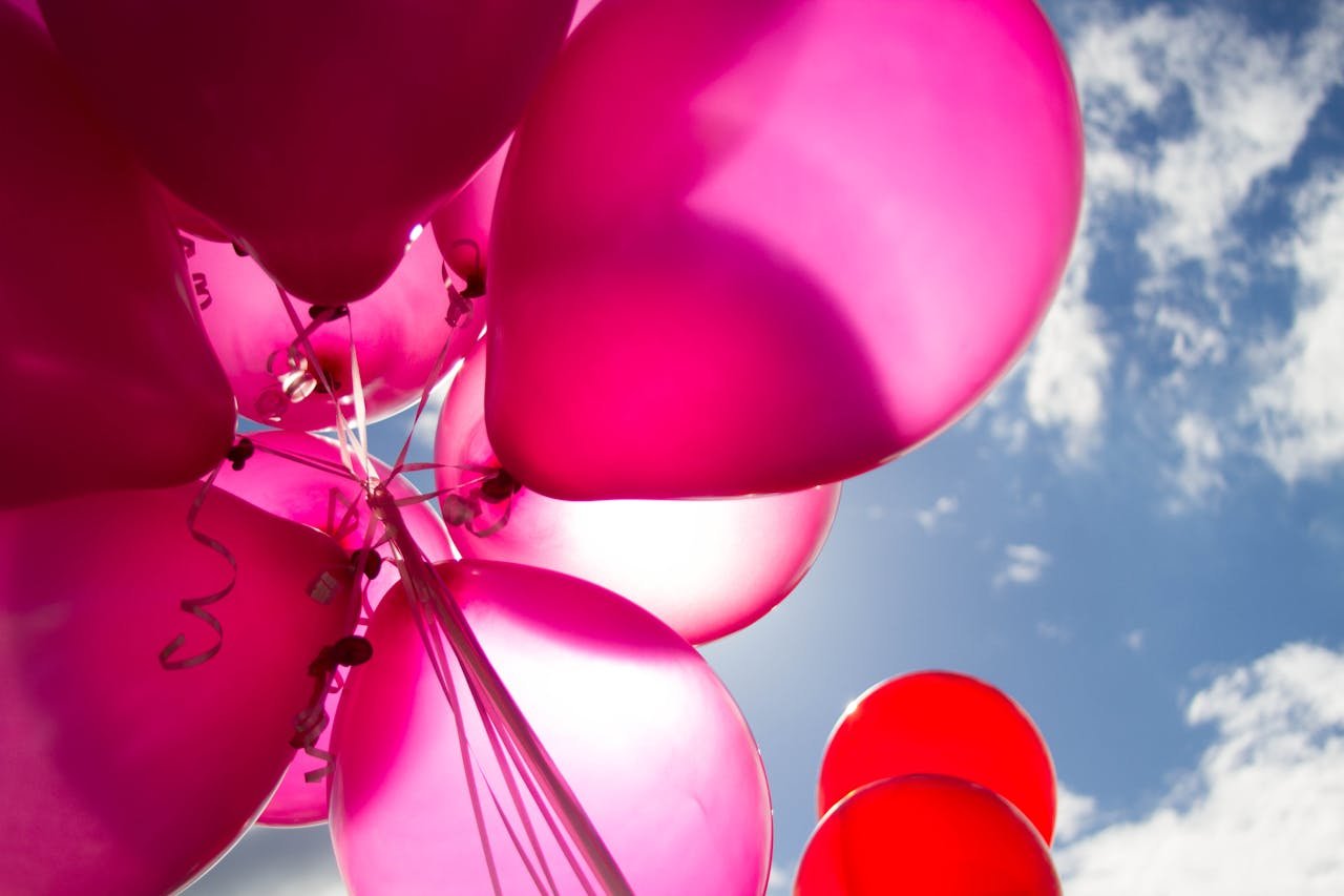 Vibrant pink balloons float against a sunny blue sky, perfect for celebratory themes.